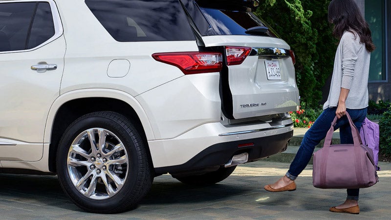 A lady using the hands-free sensing feature to open the trunk of a Chevrolet Traverse, holding a bag in both hands.