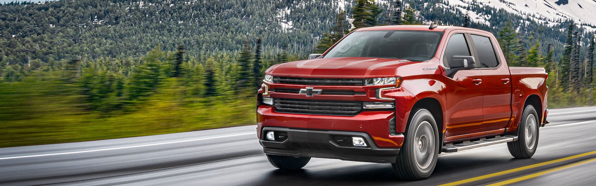 Chevrolet Silverado 1500 driving on a road with mountains and trees.
